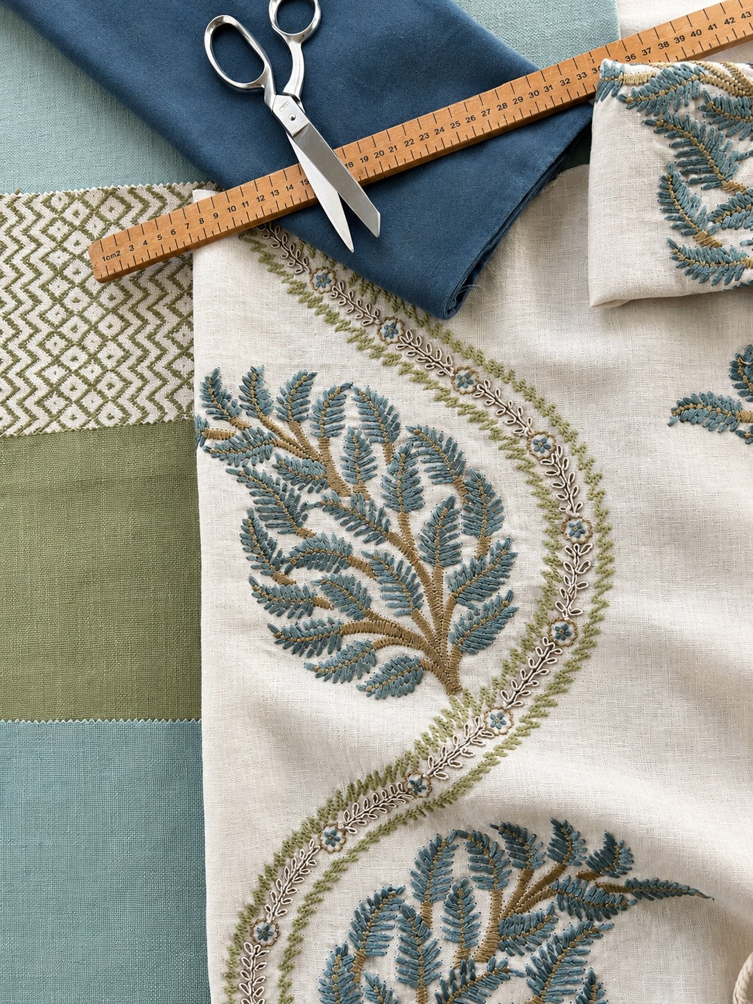 Blue and green fabric samples with embroidered linen, a wooden ruler and dressmaking shears